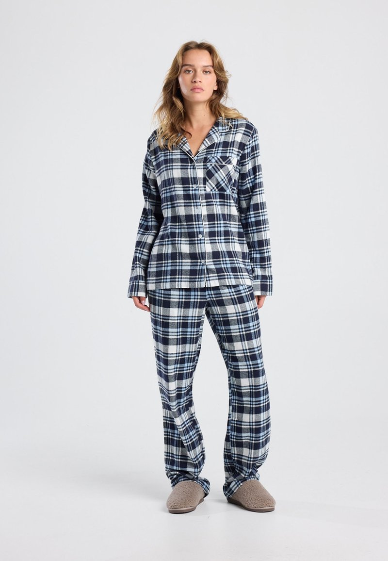 Flannel pajama set in navy and white plaid, featuring long sleeves, button closure, chest pocket, and relaxed-fit pants with matching pattern.