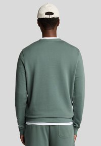 Felpa verde con scollo a girocollo e polsini a coste, abbinata a pantaloni coordinati. Tessuto morbido, design informale e orlo bianco a strati.
