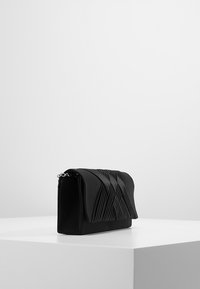 Černá psaníčko z měkké látky s plisovaným designem, uzavíratelná klopou a stříbrným kováním. Čtvercový tvar s minimalistickým stylem.