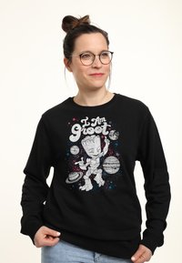 Sudadera negra con un gráfico de un personaje de dibujos animados rodeado de planetas y estrellas con el texto "Yo soy Groot" en letras negritas.