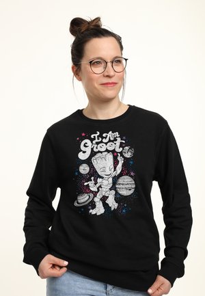Sudadera negra con un gráfico de un personaje de dibujos animados rodeado de planetas y estrellas con el texto "Yo soy Groot" en letras negritas.