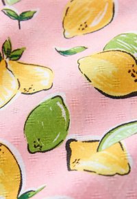 Tissu avec un fond rose texturé mettant en scène des citrons jaunes, des citrons verts et des feuilles vertes éparpillées dans un motif imprimé.