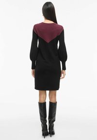Czarna dzianinowa sukienka z bordowym wzorem w kształcie szewrona z tyłu, długimi bufiastymi rękawami i prostym dołem. Do tego czarne kozaki za kolano.