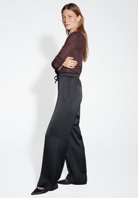Pantaloni larghi in satin nero con vita elastica e cordoncino, abbinati a una maglietta a maniche lunghe bordeaux con texture.