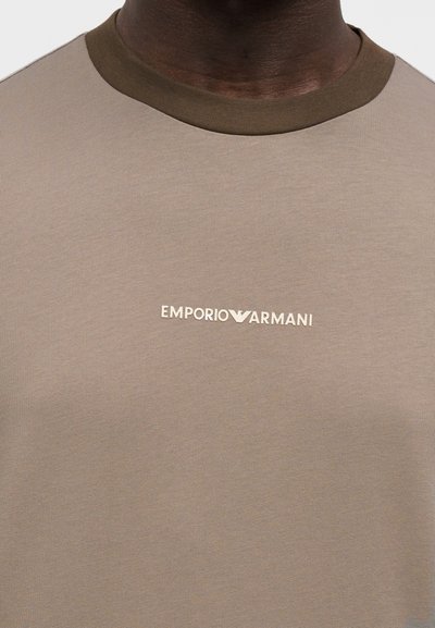 Μπλούζα με κοντά μανίκια σε μπεζ χρώμα, κατασκευασμένη από λείο ύφασμα, με αντιθετικό χακί λαιμόκοψη και μικρό λευκό λογότυπο Emporio Armani στο στήθος.
