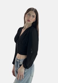 Schwarzes, kurzes Oberteil mit V-Ausschnitt, gepufften langen Ärmeln und Knopfdetail vorne. Kombiniert mit hellblauen, hoch taillierten Jeans.