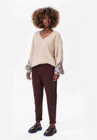 Beżowy, oversize sweter z dekoltem w serek, z wzorzystymi mankietami, w połączeniu z ciemno-brązowymi, zwężanymi spodniami i masywnymi loafersami. Gładkie, przytulne faktury.