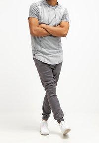 Maglietta grigia a maniche corte con cappuccio e motivo sfumato, abbinata a pantaloni jogger grigi con polsini elastici, indossata con sneakers bianche.