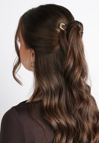 Capelli castani ondulati acconciati con una clip dorata, caratterizzati da una texture liscia e un design half-up, half-down.