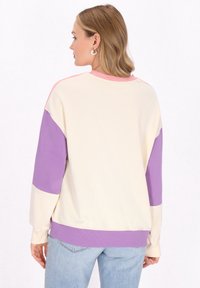 Felpa a maniche lunghe color block in crema, rosa e viola. Tessuto morbido, scollatura rotonda, maniche lunghe e rib di finitura sui polsini e sull'orlo.