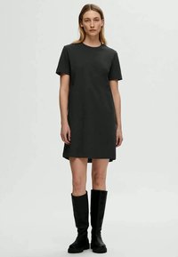 Rochie din bumbac negru, cu o croială lejeră, decolteu rotund, mâneci scurte și fante pe laterale, completată cu cizme negre până la genunchi.