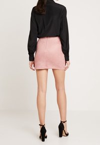 Chemise noire à manches longues associée à une mini-jupe en suède rose. La tenue présente une coupe ajustée et des chaussures noires à talons hauts.