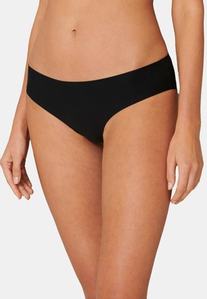 Bauchbereich einer Frau, die nahtlose schwarze Bikini-Unterwäsche trägt, vor einfachem Hintergrund.