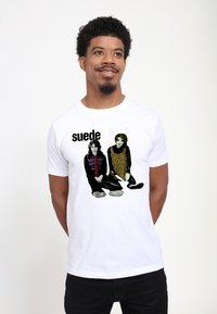 Hvid bomulds t-shirt med trykt grafik af to siddende figurer. Designet inkluderer teksten "suede" og farverige accenter på tøjet.