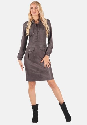 Graues Kunstwildlederkleid mit Kragen, vorderer Schnürung und zwei Brusttaschen. Lange Ärmel und taillierte Silhouette. Schwarze Knöchelschäfte.