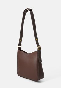 Sac à épaule en cuir marron avec un haut arrondi et une surface texturée. Il dispose d'une longue bandoulière avec des coutures blanches et des accents en métal doré.