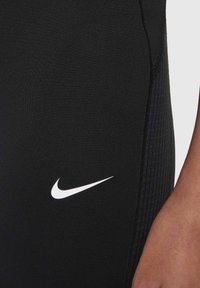 Leggings sportivi neri realizzati in tessuto elastico, con il logo Nike bianco sul davanti e pannelli laterali texturizzati per un tocco di dettaglio in più.