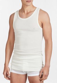 Top bianco di cotone morbido, caratterizzato da un classico collo rotondo e ampie aperture per le braccia, abbinato a pantaloni corti bianchi aderenti sottostanti.