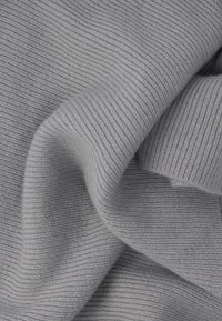 Ανοιχτό γκρι πλεκτό ύφασμα με ριμπ υφή, που παρουσιάζει απαλές πτυχώσεις και ρευστότητα, αναδεικνύοντας ομοιόμορφη, λεία ραφή σε όλο το ύφασμα.