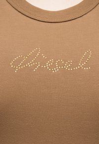 Κοντινό πλάνο καφέ ριγωτού υφάσματος τοπ με τη λέξη "allegro" γραμμένη με μικρές χρυσές καρφίτσες στην περιοχή του στήθους.