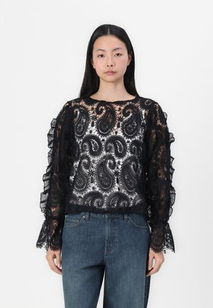 Schwarze Spitzenbluse mit Paisleymuster, Rüschensleeves und einem durchscheinenden, strukturierten Design. Kombiniert mit blauen Jeans.