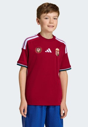 Maglia sportiva rossa con dettagli bianchi e verdi, con lo stemma dell'Ungheria e una spilla circolare. Realizzata in tessuto traspirante, con scollo rotondo.