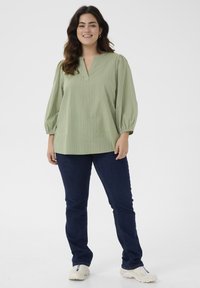 Ljusgrön, randig blus med V-ringning och puffärmar, i kombination med mörkblå jeans. Outfitten avslutas med vita sneakers.