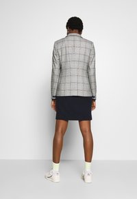 Blazer de cuadros en gris con acentos en azul y negro, combinado con una falda azul marino. Presenta un corte estructurado y botones, usado con zapatillas blancas y calcetas a rayas.