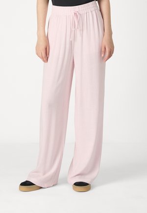 Pantalons larges de couleur rose clair en tissu doux avec une taille élastique et un cordon de serrage. Associés à des chaussures noires à semelle légère.
