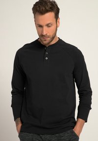 Musta pitkähihaisuus henley-paita, jossa on pyöreä kaula-aukko ja kolme napin placketia. Pehmeä kangas, jossa on sileä tekstuuri ja vartalonmyötäinen siluetti.