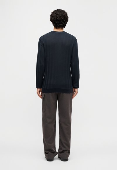 Μπλούζα μακρυμάνικη σε σκούρο ναυτικό χρώμα με υφή ψαροκόκκαλου, συνδυασμένη με άνετο γκρι παντελόνι. Απλός λαιμός τύπου crew και χωρίς ορατά λογότυπα.