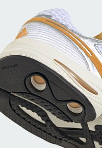 Gros plan sur la semelle d'une chaussure de sport blanche et orange montrant la bande de roulement en caoutchouc noir et les trous de coussin d'air.