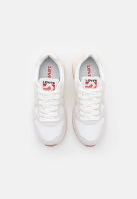 Baskets Levi's avec une tige en maille et cuir blanc, accentuées de beige, lacets blancs et détails du logo rouge sur la languette. Semelle en caoutchouc.