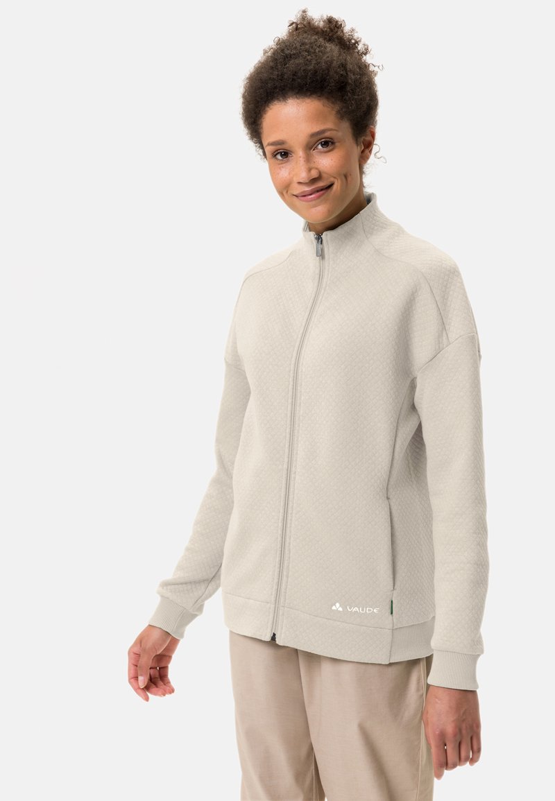 Sweatshirt zippé gris clair en tissu texturé. Il présente un col montant, des poignets côtelés et un petit logo en bas à gauche.