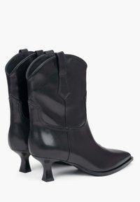 Czarne skórzane botki za kostkę o błyszczącym wykończeniu, w szpic, z zaokrąglonym górnym brzegiem i niskim blokowym obcasie. Posiadają delikatne przeszycia i boczne pętle.