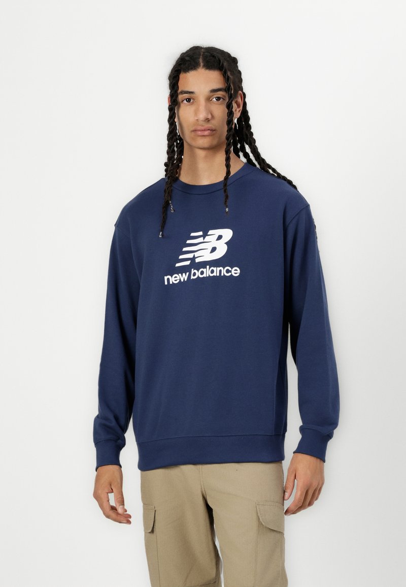 Tumši zils kokvilnas džemperis ar apaļu kakla izgriezumu, garām piedurknēm un balto "new balance" logo uz krūtīm. Iekļautas ribotas aproces un apakšmalas.
