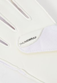 Weißer Handschuh mit strukturierter Oberfläche, ausgestattet mit einem Daumenschutzetikett. Das Design umfasst Schlitze zur Belüftung und ein glattes, flexibles Material.