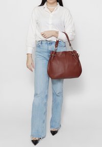 Sac à main en cuir marron au design souple avec des détails en métal argenté. Le sac possède une poignée courte et une texture lisse.