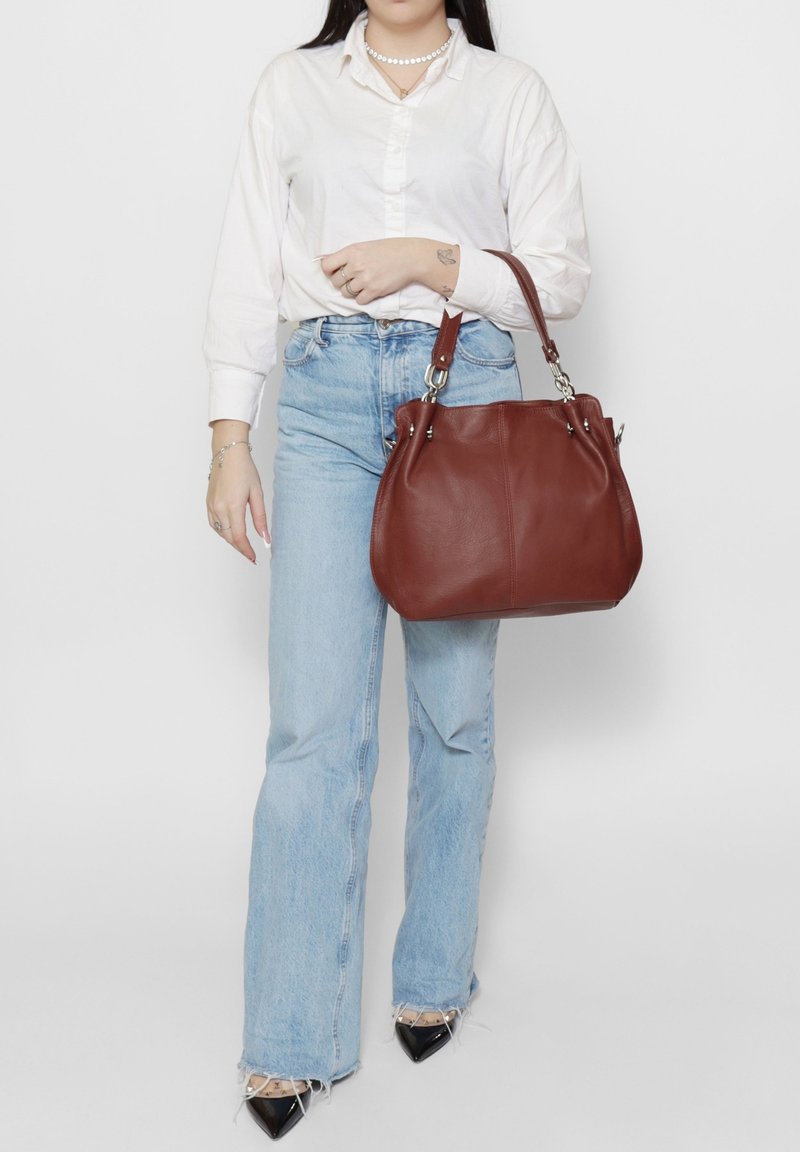 Sac à main en cuir marron au design souple avec des détails en métal argenté. Le sac possède une poignée courte et une texture lisse.