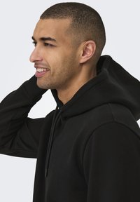 Felpa nera con cappuccio realizzata in un tessuto misto cotone. Caratterizzata da una tasca a marsupio e cappuccio con coulisse, con polsini e orlo a coste.