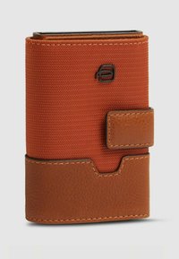 Cartera vertical hecha de tela naranja con una base de cuero marrón texturizado. Cuenta con un cierre magnético y un detalle del logo en relieve.