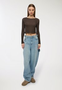 Brązowy krótki top z długim rękawem, jasnoniebieskie luźne dżinsy z pętelkami na pasek oraz brązowe obuwie. Dżinsy mają luźny krój i wyraźne kieszenie.