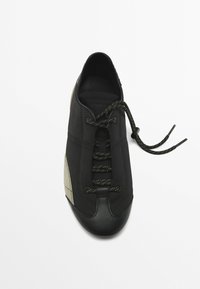 Czarne sneakersy z tkaninowym wierzchem i strukturalnym beżowym akcentem z boku. Posiadają czarne sznurówki i zaokrąglony design czubka.