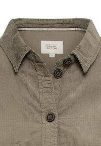 Chemise en velours côtelé marron clair avec un col pointu, des boutons à l'avant et une doublure intérieure colorée. Inclut une étiquette avec des informations de taille.