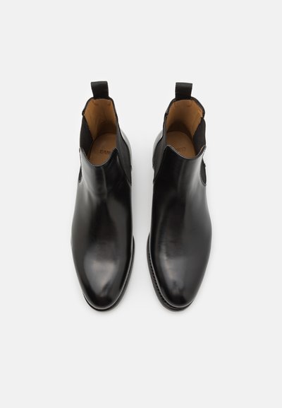 Botas de tobillo de cuero negro con un acabado liso, paneles laterales elásticos y lengüetas para facilitar su puesta. Diseño moldeado con punta redondeada.