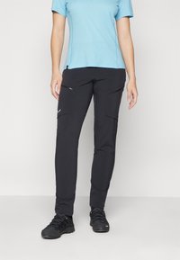 Calças pretas com bolsos de carga e fechos zíper, feitas de um tecido leve. Combinadas com uma camisa azul de manga curta e sapatos de caminhada pretos.
