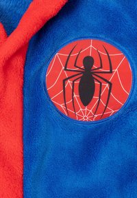 Blau-rot gefütterter Hoodie mit einem runden Patch, der ein schwarzes Spinnenmotiv und ein Netzmuster vor einem roten Hintergrund zeigt.