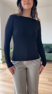 Must have pikkade varrukatega must sobiv topp, mis on kombineeritud heledate hallide laiade pükstega, millel on sile tekstuur ja lihtne disain.