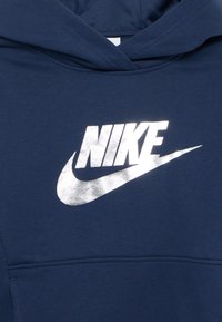 Felpa blu navy con tasca frontale, caratterizzata da un grande logo Nike riflettente in argento sul petto. Tessuto dalla texture liscia.