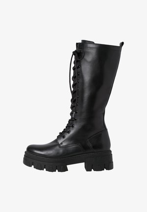 Botte de combat noire en cuir, montant jusqu'au genou, avec une semelle épaisse à crampons et une fermeture éclair à lacets sur le devant.